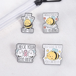 Detail view of four cartoon bee enamel pins with witty text on white fabric background