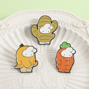Detail of cute enamel pins featuring ginger, banana, and carrot characters on a plate