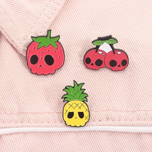 Detailed view of skull-themed strawberry, cherry, and pineapple enamel pins on pink denim