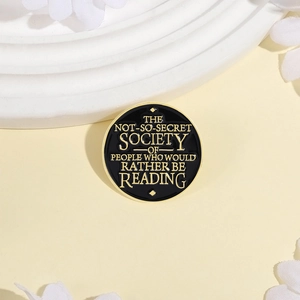 Round black enamel reading badge with gold lettering for backpacks and clothing