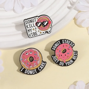 Set di tre spille in smalto a forma di ciambella con scritte su sfondo decorativo crema