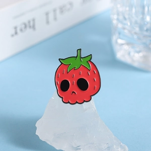 Detail shot of a strawberry skull enamel pin with vibrant red finish and green leaf accent