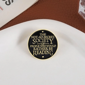 Black and gold enamel pin with inspirational book quote on a rustic textured background
