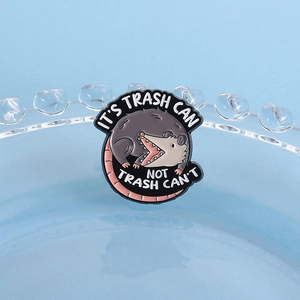 Detalle del pin redondo de esmalte con zarigüeya y texto motivador sobre fondo azul claro