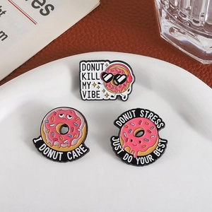 Tre spille smaltate a forma di donut con slogan mostrate in un piatto bianco
