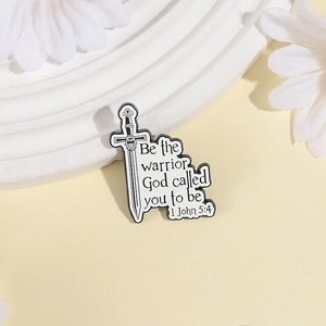 Minimalist sword enamel pin with 1 John 5:4 biblical quote on white decorative stand