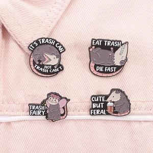 Detalle de cuatro pines de esmalte de zarigüeya con frases divertidas sobre tela rosa