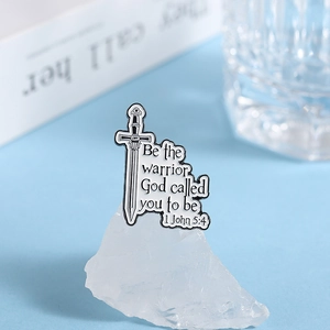 Macro detail of sword enamel pin with scripture quote Be the warrior God called you to be