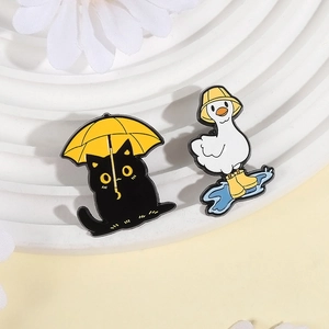 Close-up of cute enamel pins featuring a black cat with umbrella and a duck in rain gear