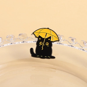 Macro d'un pin's chat noir avec parapluie jaune sur le rebord d'un plateau en verre