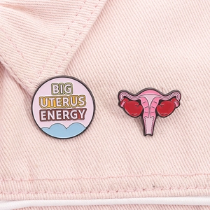 Close-up of pink Big Uterus Energy enamel pins with boxing gloves on denim fabric