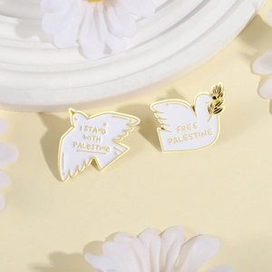 Set of two white enamel peace dove pins with Palestine support text on a bright floral setup