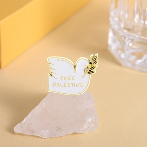 Detail view of white enamel peace dove pin with gold Free Palestine text and olive branch