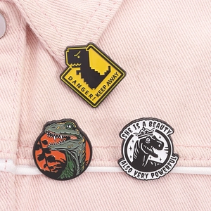 Detailed view of three dinosaur enamel pins attached to a pink denim jacket sleeve