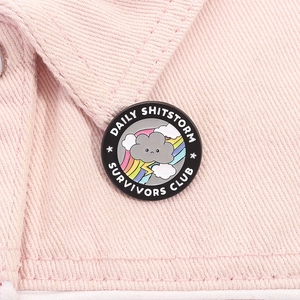 Détail d'un pin's en métal rond avec texte Daily Shitstorm Survivors Club sur denim rose