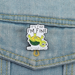 Funny green turtle enamel pin with It's Fine text pinned on blue denim jacket