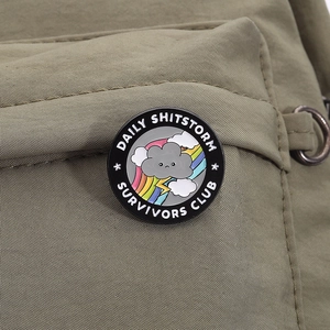 Détail d'un pin's émaillé rond avec nuage et arc-en-ciel sur un sac en toile vert
