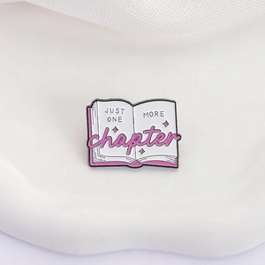 Pink open book enamel pin with 'Just One More Chapter' text on white background