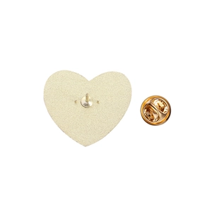 Dettaglio del retro della spilla dorata a forma di cuore con texture opaca e chiusura a farfalla