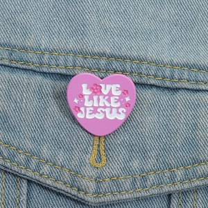 Broche cœur rose avec texte 'Love Like Jesus' fixée sur une poche de veste en jean bleue