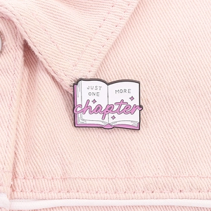 Detail of book-shaped enamel pin with Just One More Chapter text on pink denim
