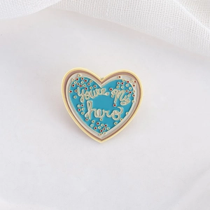 Blue heart enamel brooch with You're My Hero lettering and golden metal outlines