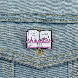 Creative pink book enamel pin with 'Just One More Chapter' text on denim jacket