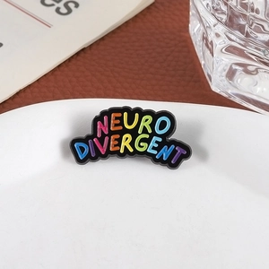 Macro shot of Neuro Divergent enamel pin with rainbow letters on white ceramic