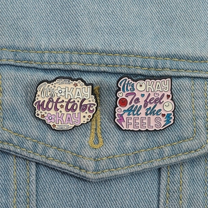 Creative It's OK enamel pin set with mental health quotes on blue denim jacket