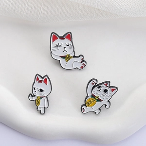 Detailed view of three white lucky cat enamel pins on stone surface with gauze