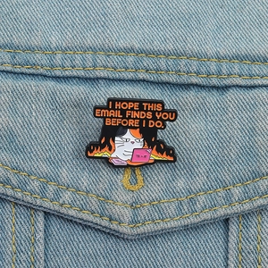 Enamel cat brooch featuring a tired calico cat working on a laptop with fire background