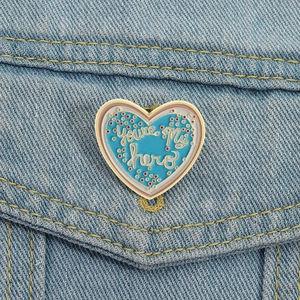 Spilla a cuore smaltata blu con scritta 'You're My Hero' su giacca denim