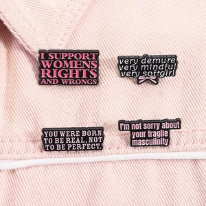 Detailed macro view of four feminist slogan enamel pins on pink denim fabric surface