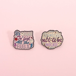 Creative enamel pins featuring motivational quotes It's OKAY on soft pink background