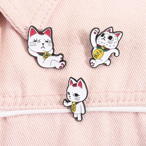 Detailed view of three cartoon lucky cat enamel pins on pink denim fabric texture