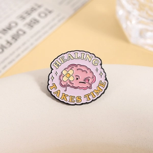 Macro detail of pink healing brain enamel pin with stars and HEALING TAKES TIME text