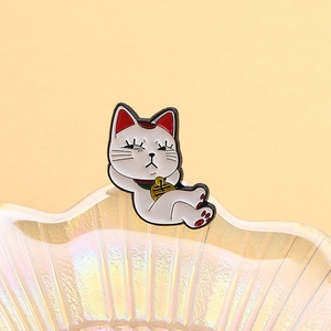 Détail macro du pin's émaillé Maneki Neko couché avec clochette dorée sur verre