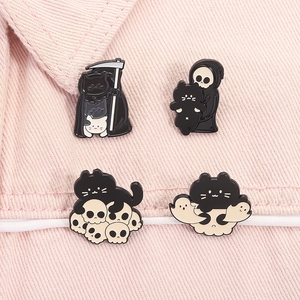 Close-up of four dark-themed Grim Reaper cat enamel pins on pink denim fabric
