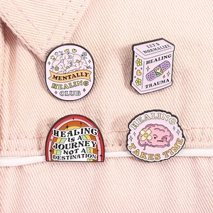 Close-up of pink enamel mental health badges with healing quotes on denim fabric