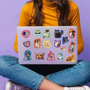 Vibrant cartoon cat stickers decorated on a laptop held by a person in a yellow sweater