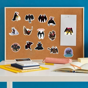 Close-up of artistic Mothman stickers on a desk with a notebook and office supplies