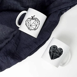 Dettaglio di due tazze in ceramica con motivi geometrici minimalisti di mela e cuore neri