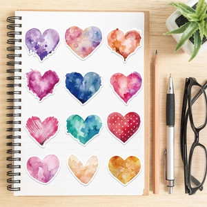Détail d'autocollants cœurs aquarelle disposés sur un carnet avec de la papeterie