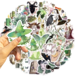 Close-up of hand holding a waterproof PVC forest witch sticker over a diverse sticker pile