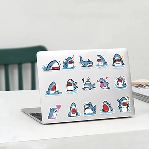 Detail view of cartoon blue shark stickers on a silver laptop with various cute expressions