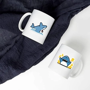 Detail of two white ceramic mugs with cute blue shark cartoons on a textured blue fabric