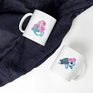 Detail of two white ceramic mugs with colorful mermaid and sea turtle cartoon prints
