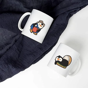 Close-up of funny penguin illustrations on two white ceramic mugs with blue fabric background