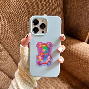 Close-up of light blue iPhone case featuring a 3D iridescent gummy bear on brown fabric