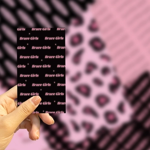 Close-up of Brave Girls pink and black decorative phone back card held by hand